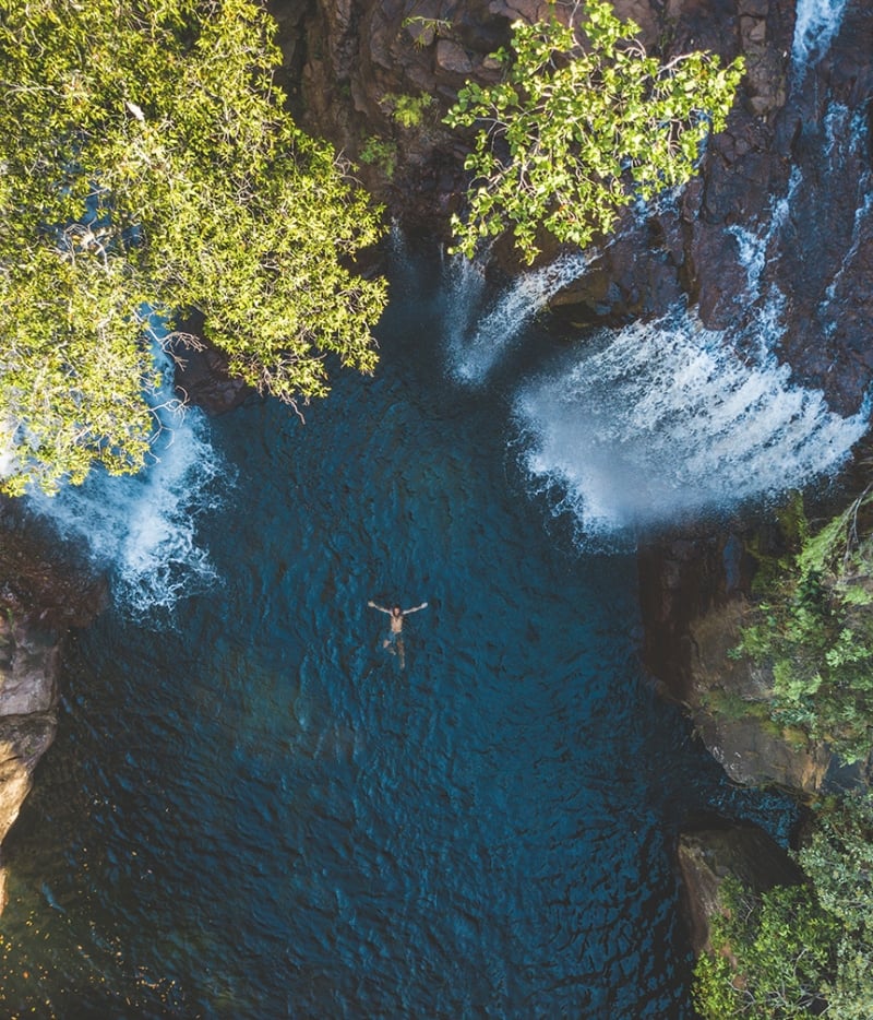 man floating in the middle of a pool below waterfalls