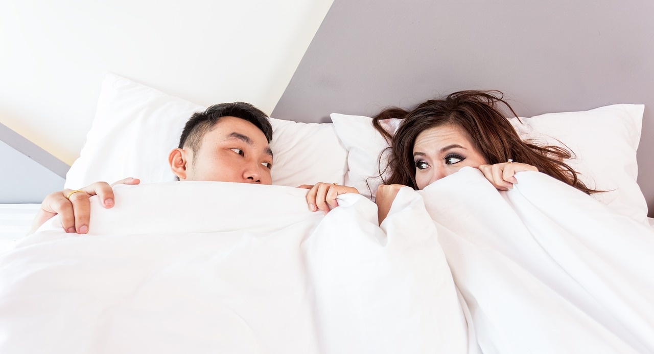 Couple under bedsheets looking intently at each other.