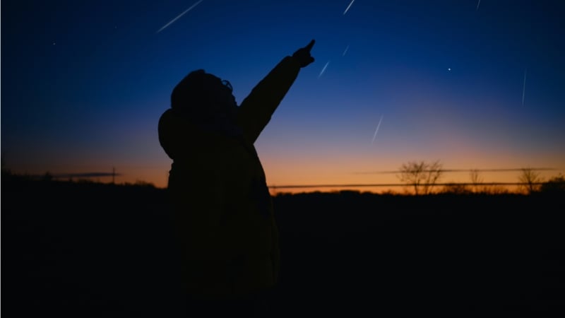 man pointing to the sky while a meteor shower occurs