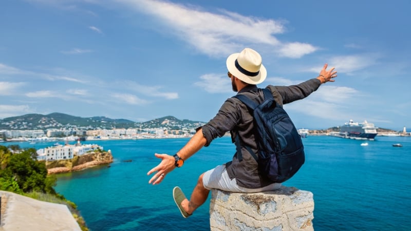 a solo traveller with his arms out wide overlooking the sea